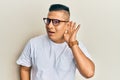 Young latin man wearing casual clothes and glasses smiling with hand over ear listening and hearing to rumor or gossip Royalty Free Stock Photo