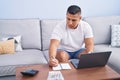 Young latin man writing on notebook accounting at home