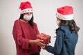 Young latin mother giving a present to her daughter on white background. Celebrating christmas wearing surgical mask during covid Royalty Free Stock Photo