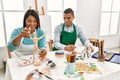 Young latin painter couple smiling happy using manikin sitting on the table at art studio Royalty Free Stock Photo