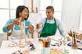 Young latin painter couple smiling happy using manikin sitting on the table at art studio Royalty Free Stock Photo