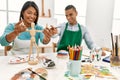 Young latin painter couple smiling happy using manikin sitting on the table at art studio Royalty Free Stock Photo