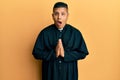 Young latin priest man praying with hands together afraid and shocked with surprise and amazed expression, fear and excited face Royalty Free Stock Photo