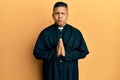 Young latin priest man praying with hands together puffing cheeks with funny face Royalty Free Stock Photo