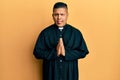 Young latin priest man praying with hands together sticking tongue out happy with funny expression Royalty Free Stock Photo