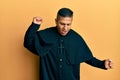 Young latin priest man standing over yellow background dancing happy and cheerful, smiling moving casual and confident listening Royalty Free Stock Photo