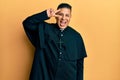 Young latin priest man standing over yellow background doing peace symbol with fingers over face, smiling cheerful showing victory Royalty Free Stock Photo