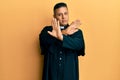 Young latin priest man standing over yellow background rejection expression crossing arms doing negative sign, angry face