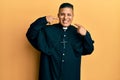 Young latin priest man standing over yellow background smiling cheerful showing and pointing with fingers teeth and mouth Royalty Free Stock Photo