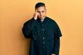 Young latin priest man standing over yellow background worried and stressed about a problem with hand on forehead, nervous and Royalty Free Stock Photo