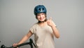 Young latin teenager female student with bicycle and blue safety bike helmet showing thumbs up smiling isolated on gray Royalty Free Stock Photo