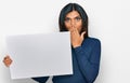 Young latin transsexual transgender woman holding blank empty banner covering mouth with hand, shocked and afraid for mistake