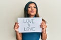 Young latin transsexual transgender woman holding paper with love is love message looking at the camera blowing a kiss being Royalty Free Stock Photo