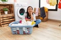 Young latin woman bored waiting for washing machine at laundry room