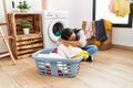 Young latin woman bored waiting for washing machine at laundry room