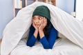 Young latin woman covering with bedsheet lying on bed at bedroom