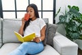 Young latin woman drinking coffee reading book at home Royalty Free Stock Photo