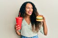 Young latin woman eating a tasty classic burger and soda smiling looking to the side and staring away thinking Royalty Free Stock Photo