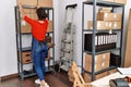 Young latin woman ecommerce business worker organizing packages on shelving at office