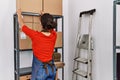 Young latin woman ecommerce business worker organizing packages on shelving at office