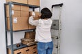 Young latin woman ecommerce business worker organizing packages shelving at office