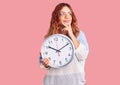 Young latin woman holding big clock serious face thinking about question with hand on chin, thoughtful about confusing idea Royalty Free Stock Photo