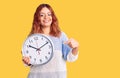 Young latin woman holding big clock smiling happy pointing with hand and finger Royalty Free Stock Photo