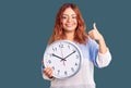 Young latin woman holding big clock smiling happy and positive, thumb up doing excellent and approval sign Royalty Free Stock Photo
