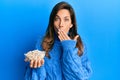 Young latin woman holding bowl with pumpkin seeds covering mouth with hand, shocked and afraid for mistake Royalty Free Stock Photo