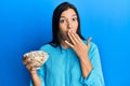 Young latin woman holding bowl with pumpkin seeds covering mouth with hand, shocked and afraid for mistake Royalty Free Stock Photo