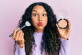 Young latin woman holding makeup brush and blush puffing cheeks with funny face