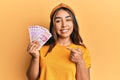 Young latin woman holding mexican pesos banknotes smiling happy pointing with hand and finger