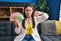 Young latin woman holding norwegian money with angry face, negative sign showing dislike with thumbs down, rejection concept Royalty Free Stock Photo