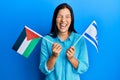 Young latin woman holding palestine and israel flags smiling and laughing hard out loud because funny crazy joke Royalty Free Stock Photo