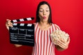 Young latin woman holding video film clapboard and popcorn making fish face with mouth and squinting eyes, crazy and comical Royalty Free Stock Photo