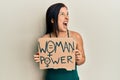 Young latin woman holding woman power banner angry and mad screaming frustrated and furious, shouting with anger