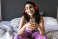 Young latin woman listening music with headphones and drinking orange juice on bed at home in Mexico Latin America Royalty Free Stock Photo