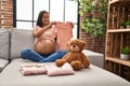 Young latin woman pregnant holding baby clothes at home Royalty Free Stock Photo