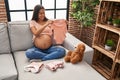 Young latin woman pregnant holding baby clothes at home Royalty Free Stock Photo