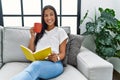 Young latin woman reading book drinking coffee at home Royalty Free Stock Photo