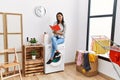Young latin woman reading book waiting for washing machine at laundry room Royalty Free Stock Photo