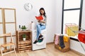 Young latin woman reading book waiting for washing machine at laundry room Royalty Free Stock Photo