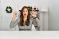 Young latin woman sitting on the table by christmas decor looking surprised and shocked doing ok approval symbol with fingers Royalty Free Stock Photo