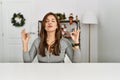 Young latin woman sitting on the table by christmas decor relaxed and smiling with eyes closed doing meditation gesture with Royalty Free Stock Photo