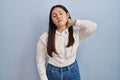 Young latin woman standing over blue background suffering of neck ache injury, touching neck with hand, muscular pain Royalty Free Stock Photo