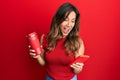 Young latin woman using smartphone and drinking a cup of coffee celebrating crazy and amazed for success with open eyes screaming Royalty Free Stock Photo