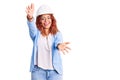 Young latin woman wearing architect hardhat looking at the camera smiling with open arms for hug Royalty Free Stock Photo