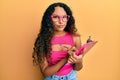 Young latin woman wearing business clothes writing on clipboard skeptic and nervous, frowning upset because of problem Royalty Free Stock Photo