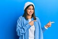 Young latin woman wearing cute wool cap pointing aside worried and nervous with both hands, concerned and surprised expression