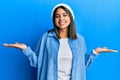 Young latin woman wearing cute wool cap smiling showing both hands open palms, presenting and advertising comparison and balance Royalty Free Stock Photo